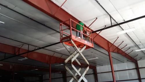 A man is standing on a scissor lift cleaning the ceiling of a building.