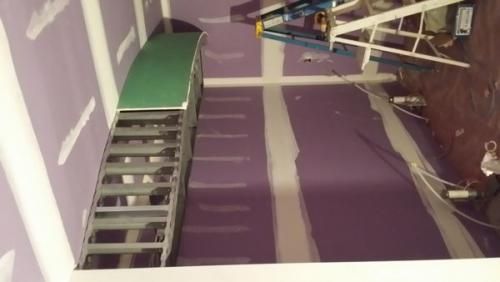 A person is standing on a ladder in a room with purple walls.