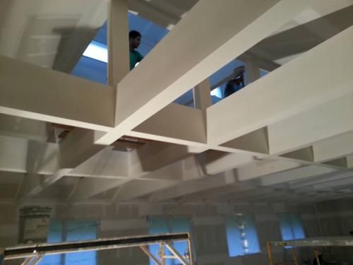 A man in a green shirt is looking up at the ceiling of a building under construction.
