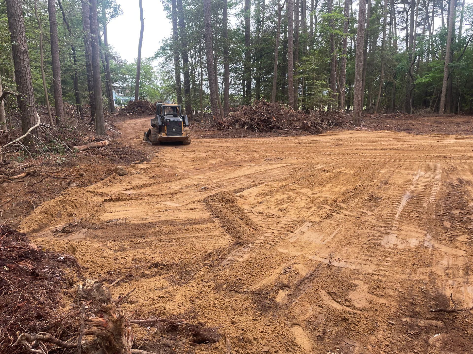 Small tractor grading a dirt clearing beside a wooded tree line