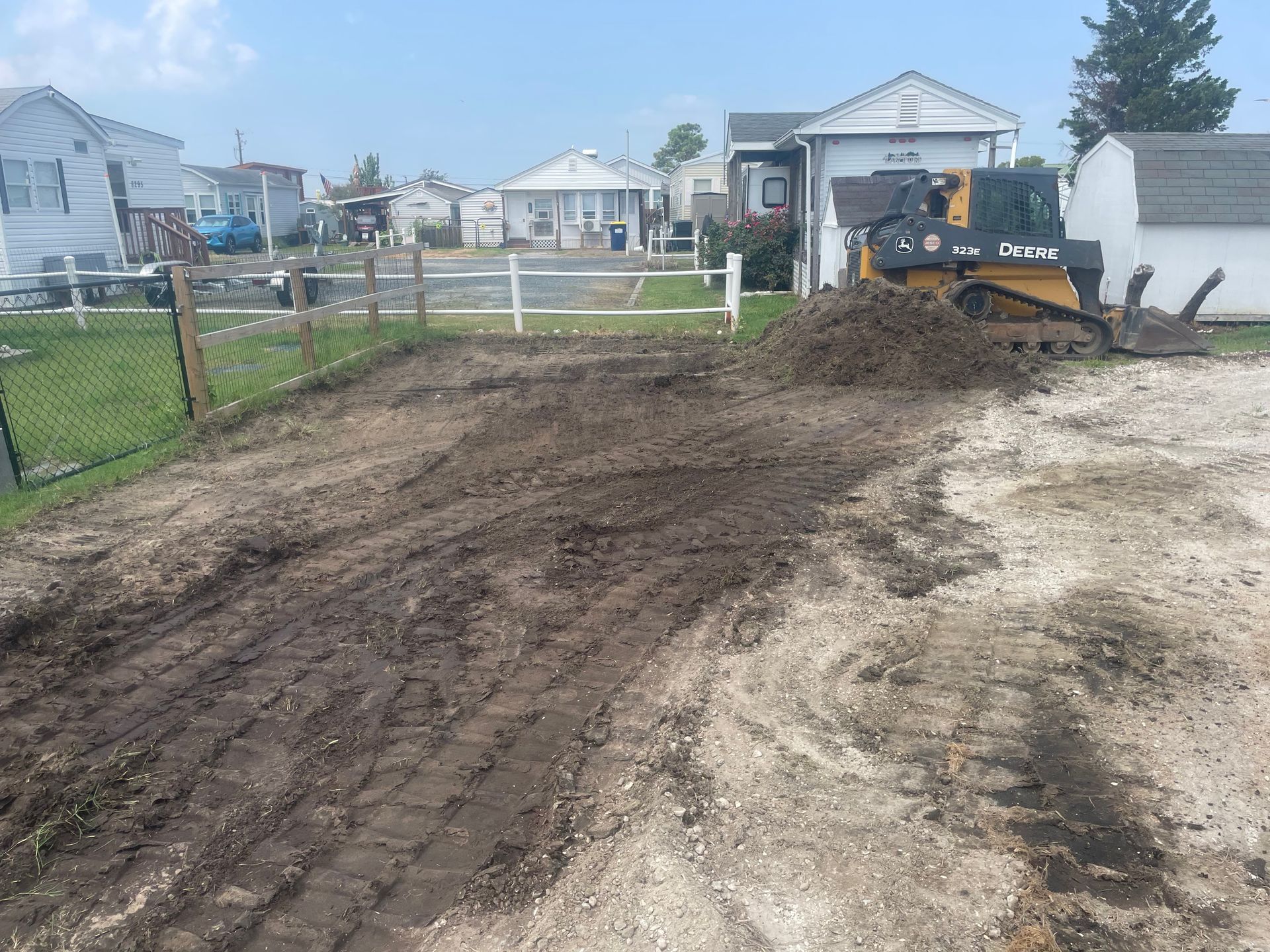 Bulldozer grading dirt in a residential yard beside a chain-link fence and houses