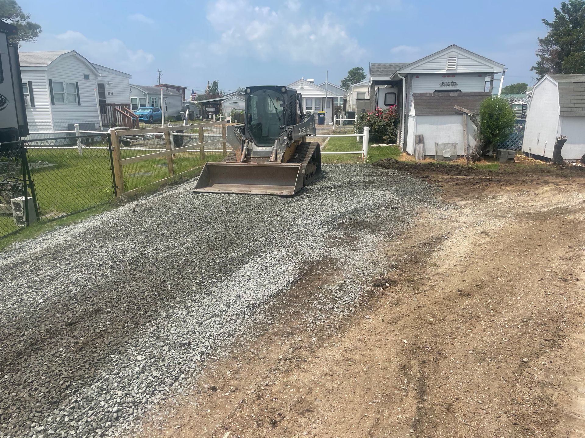 Gravel driveway with a small utility trailer in a residential neighborhood under a partly cloudy sky