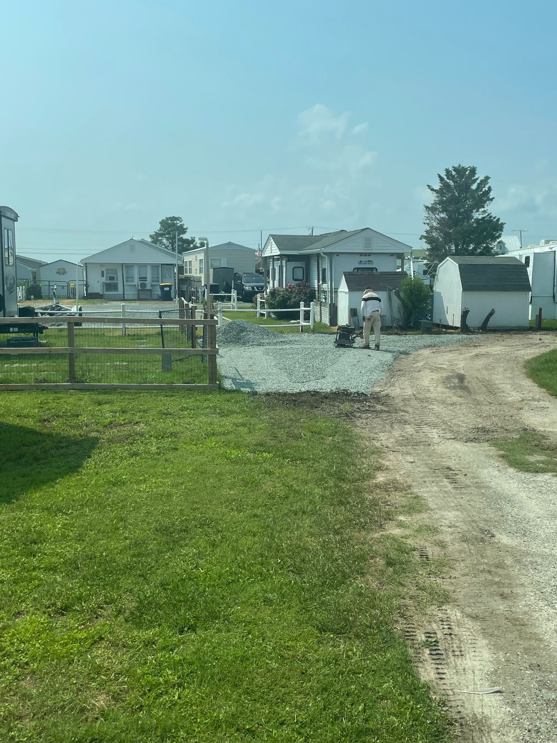 Gravel driveway leading to white houses and a gate beside a grassy yard on a sunny day