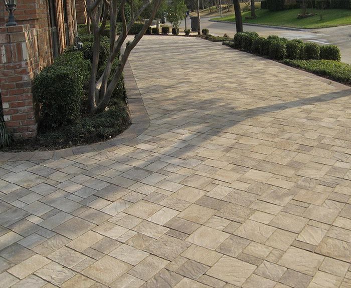A brick driveway leading to a house with bushes and trees