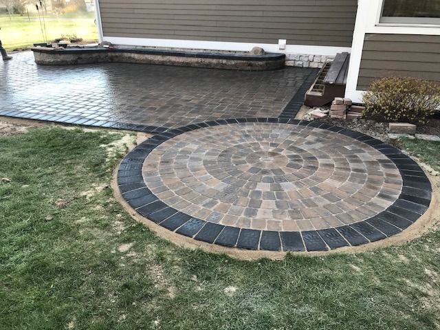 A brick patio with a circular design in the middle of it in front of a house.