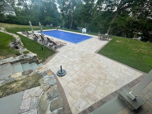 A large swimming pool is surrounded by a patio with chairs and umbrellas.