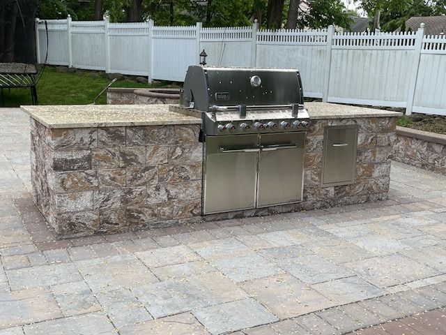 A grill is sitting on top of a stone counter on a patio.