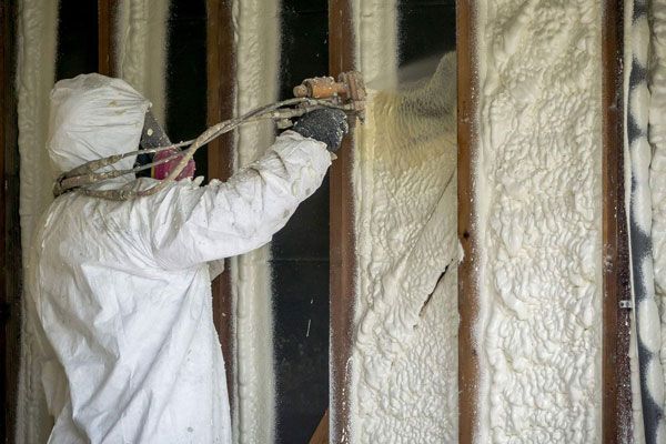 A man is spraying foam insulation on a wall.