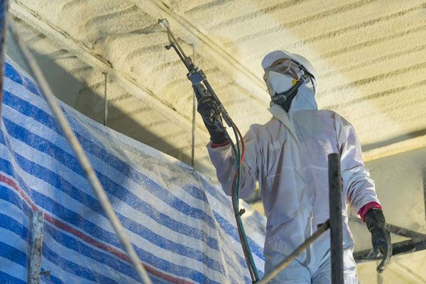 A man in a protective suit is spraying foam on a ceiling.