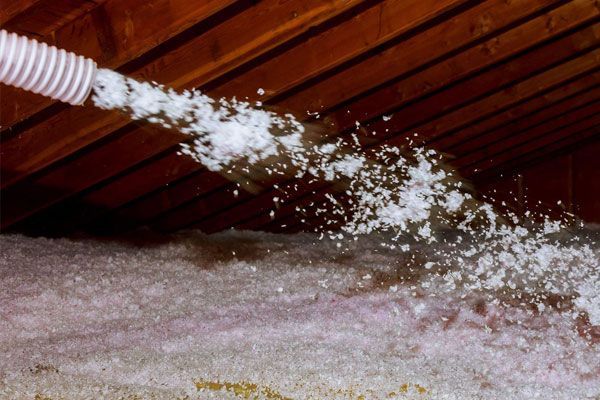 A hose is spraying white foam into an attic.