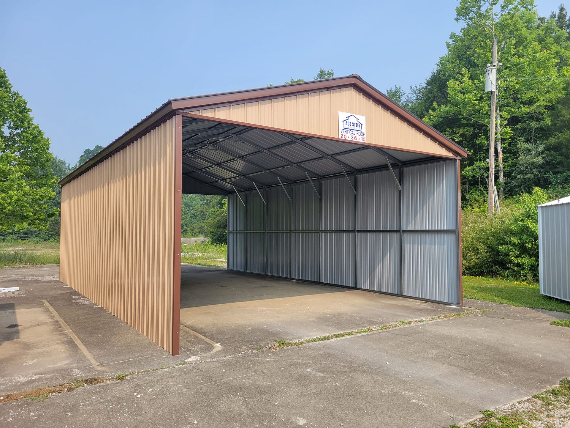 Tan and brown metal carport on concrete, open to the front, in front of trees under a blue sky.