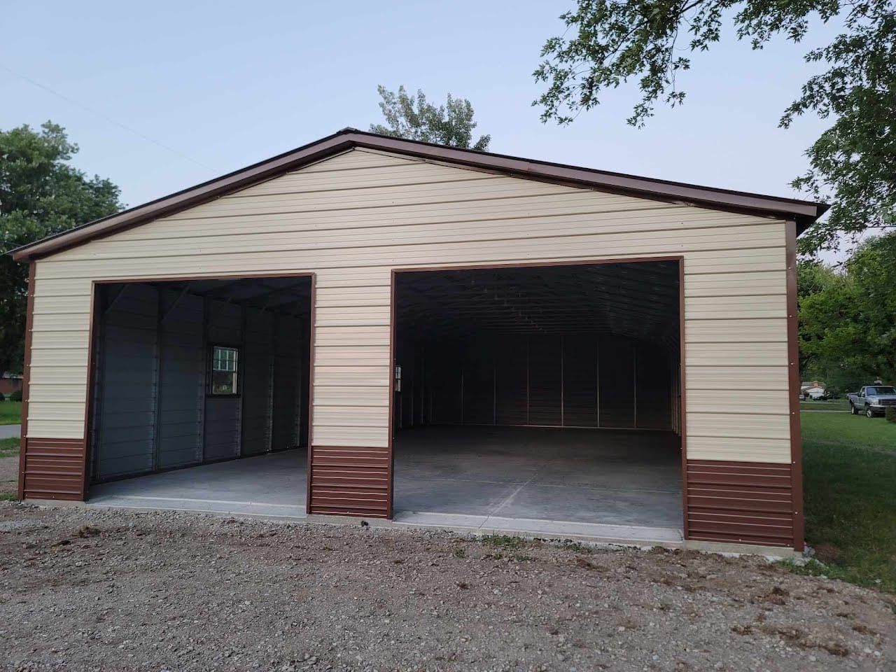 Tan and brown two-bay garage with open doors and concrete floor; gravel driveway.