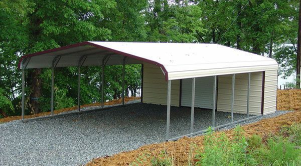 Carport with tan metal siding and gravel driveway, set against a backdrop of trees.