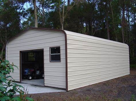 Tan metal shed with open garage door, window, and brown trim, set in a wooded area.