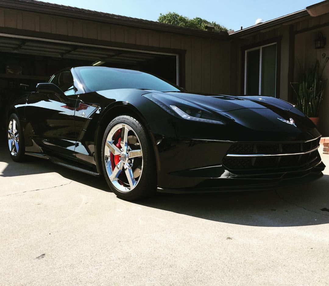 Black convertible sports car parked in front of a garage, shiny chrome wheels with red brake calipers.