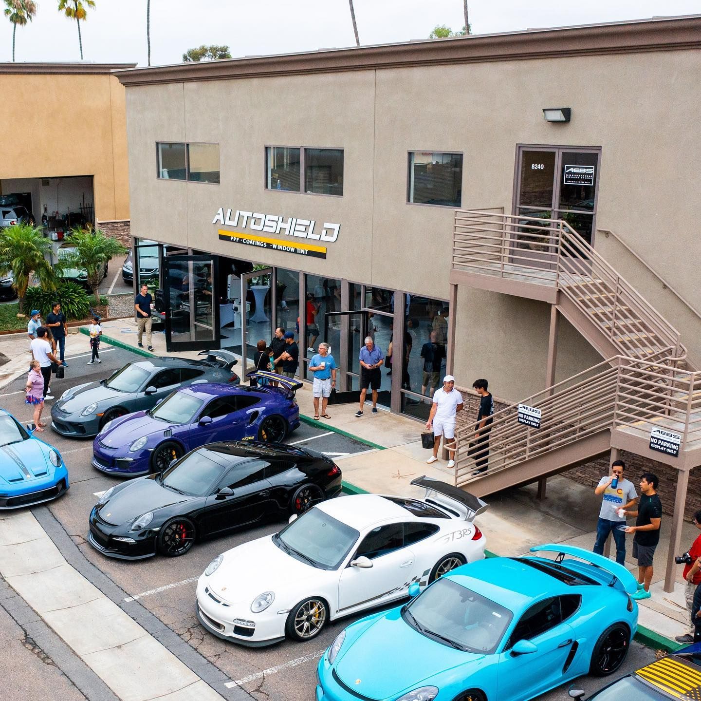 Porsche sports cars parked in front of Autoshield building, with people standing around.