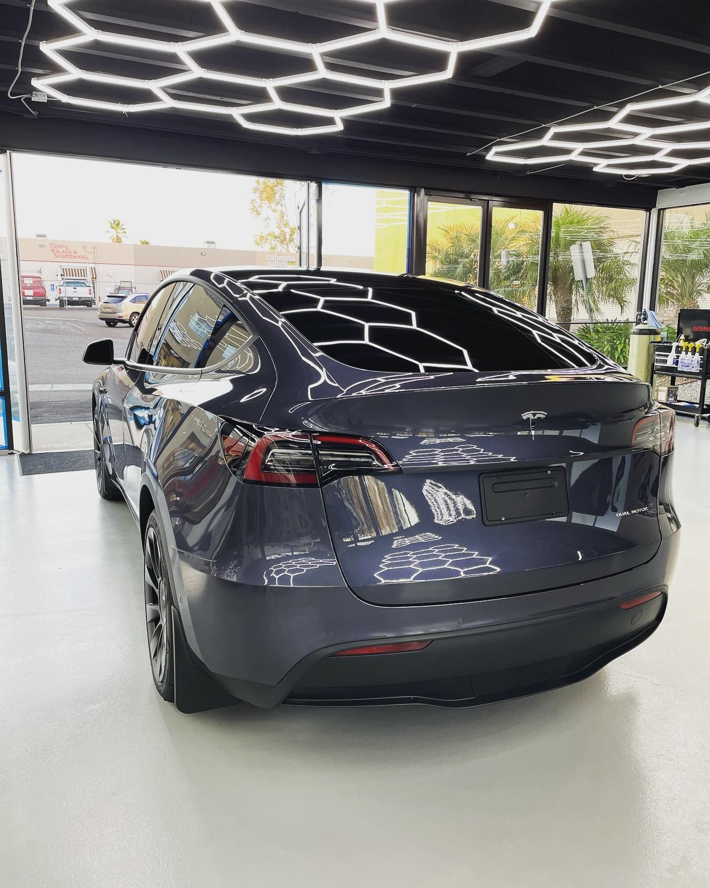 Dark gray Tesla Model Y car parked inside a shop with hexagon-shaped lights on the ceiling.