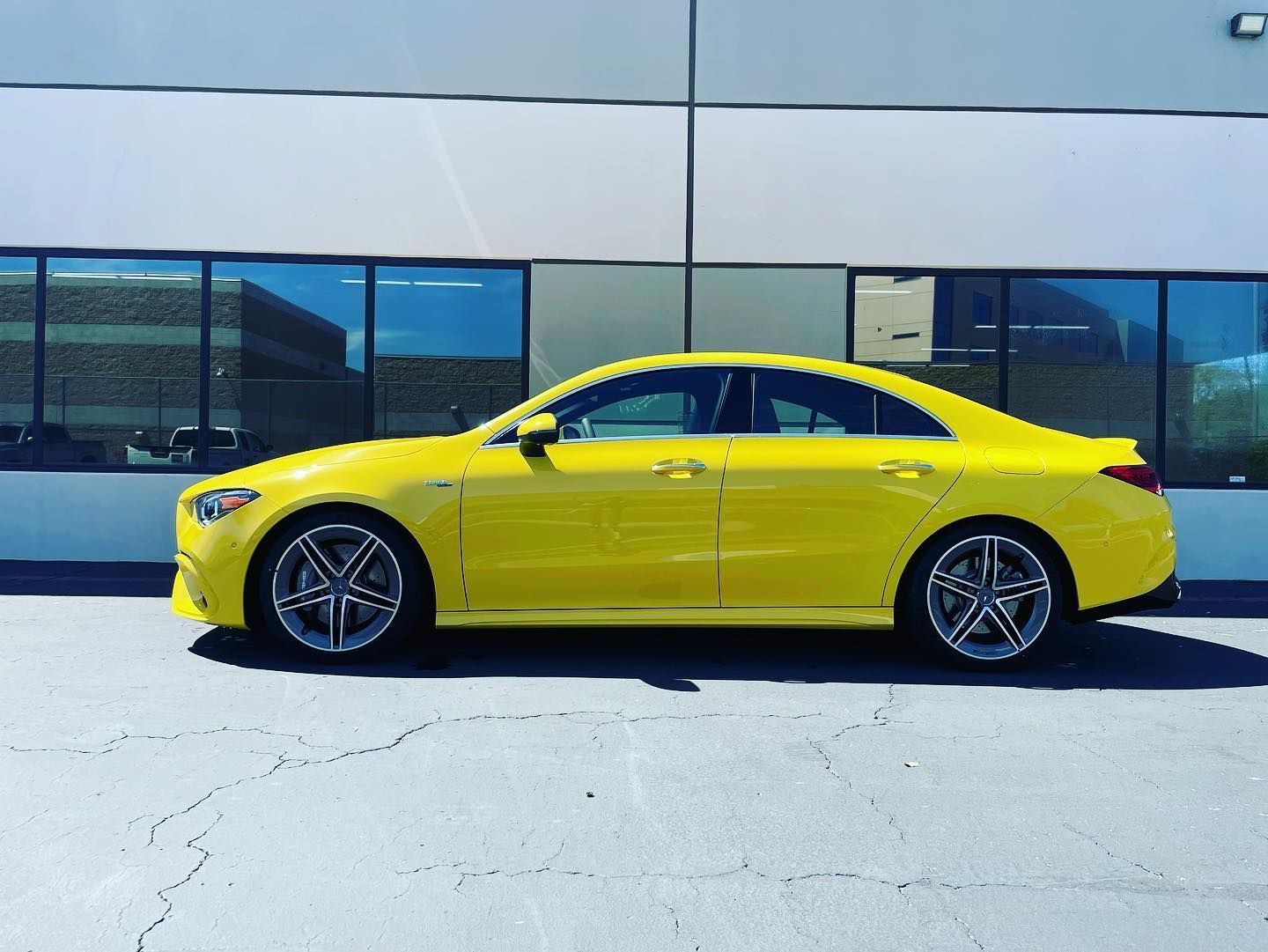 Yellow sedan parked in front of a building with glass windows, sunny day.