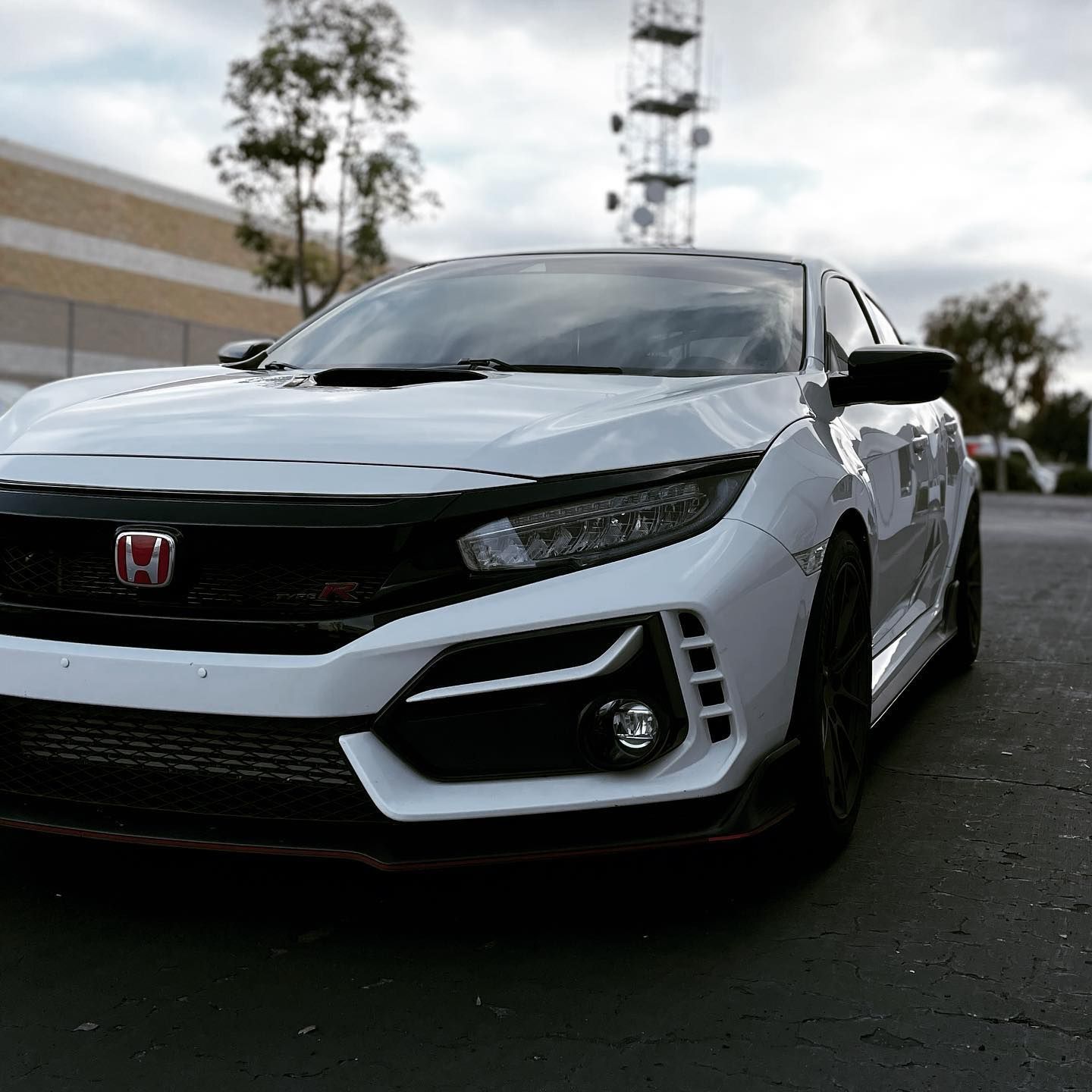 White Honda Civic Si, black accents, parked on asphalt. Red Honda emblem. Radio tower in background.
