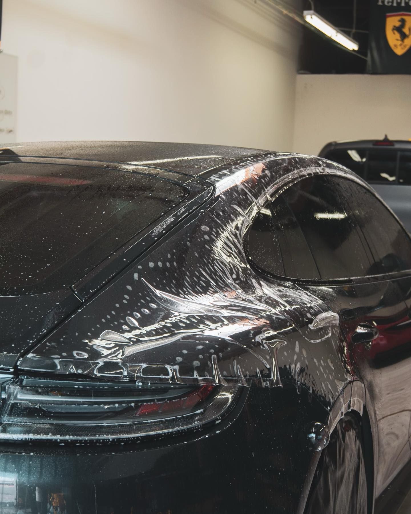 Black car getting window film applied, shop setting.