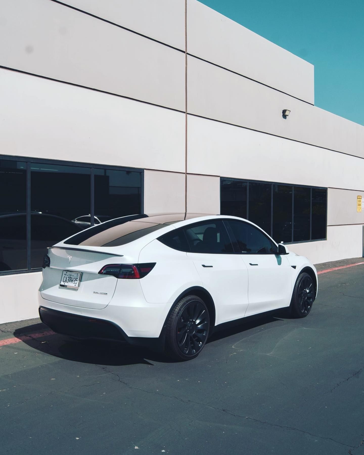 White Tesla Model Y parked in front of a modern building with large windows.