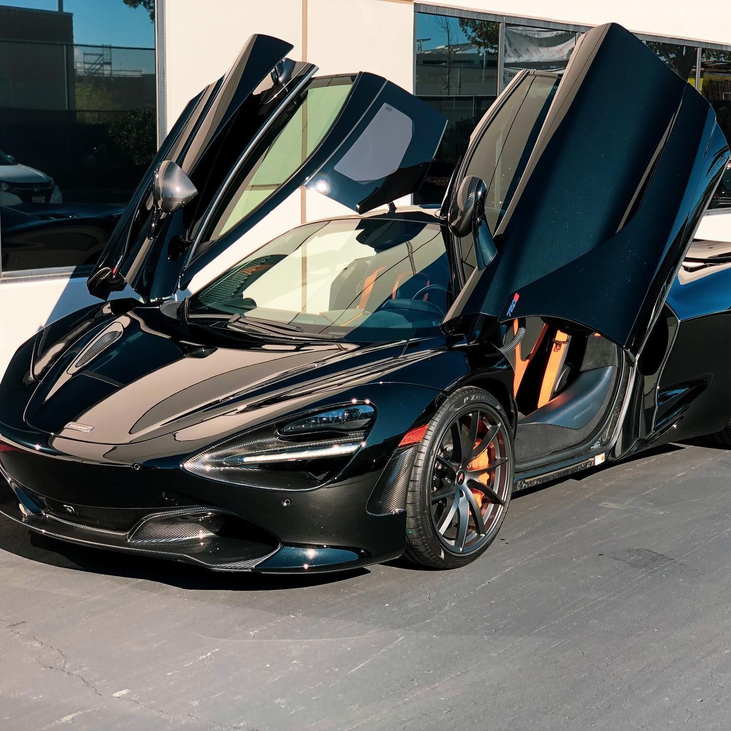 Black McLaren sports car with doors open, parked outside.