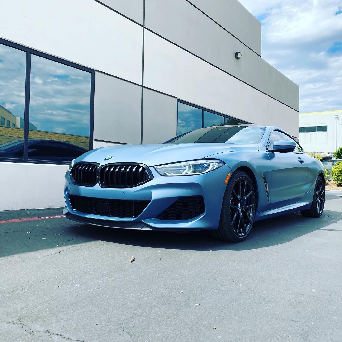 Blue BMW coupe parked in front of a modern building with reflective windows.
