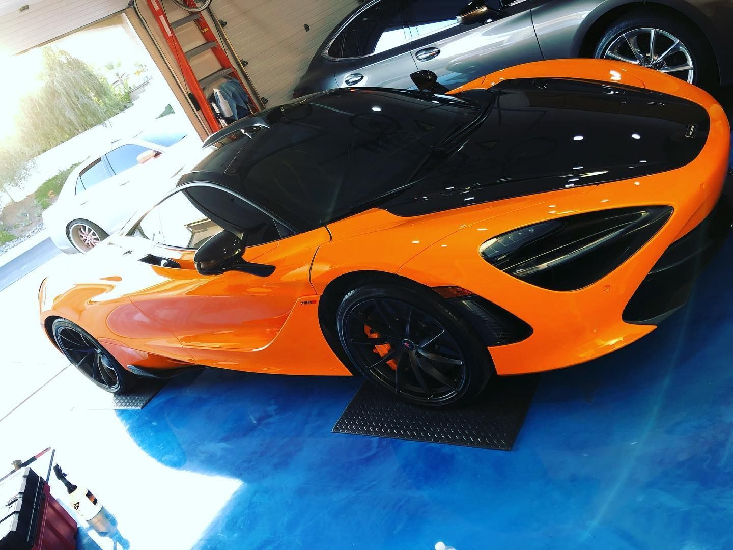 Orange and black McLaren sports car parked on a blue floor inside a garage.