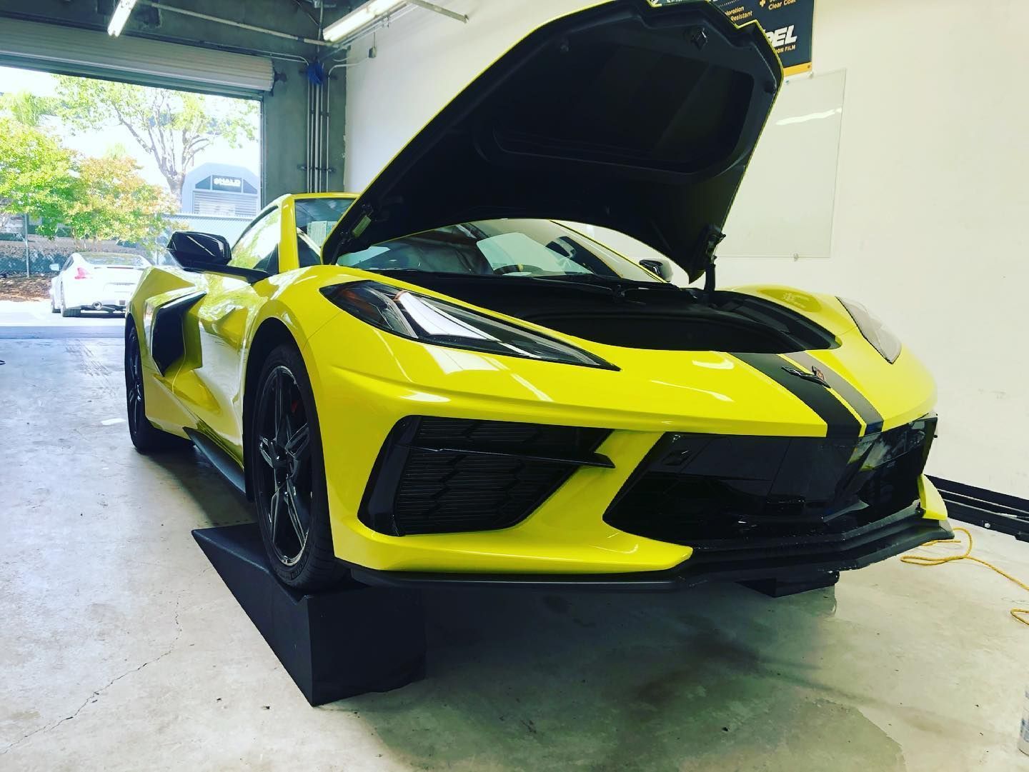 Yellow Corvette sports car with the hood open, parked in a garage.
