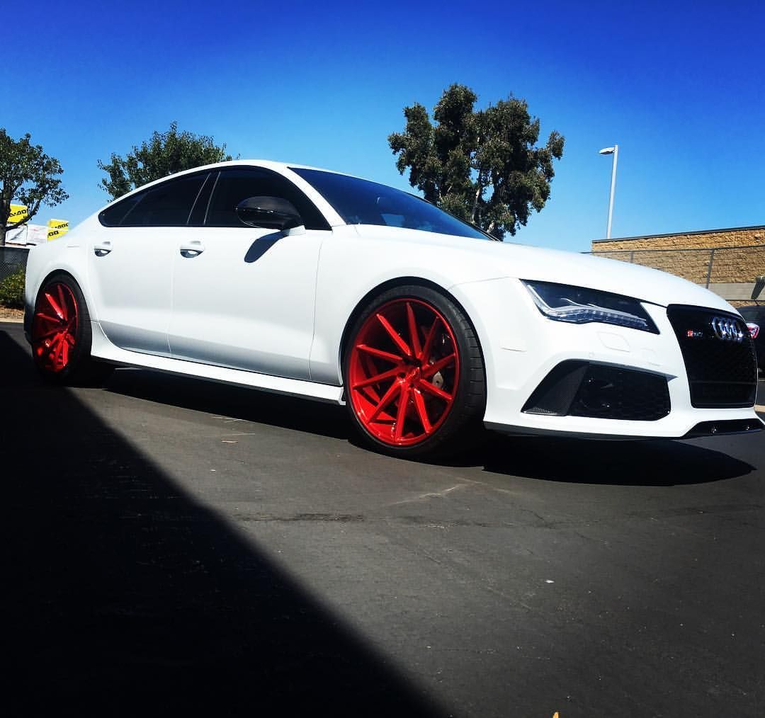 White Audi RS7 with red rims parked on asphalt under a blue sky.
