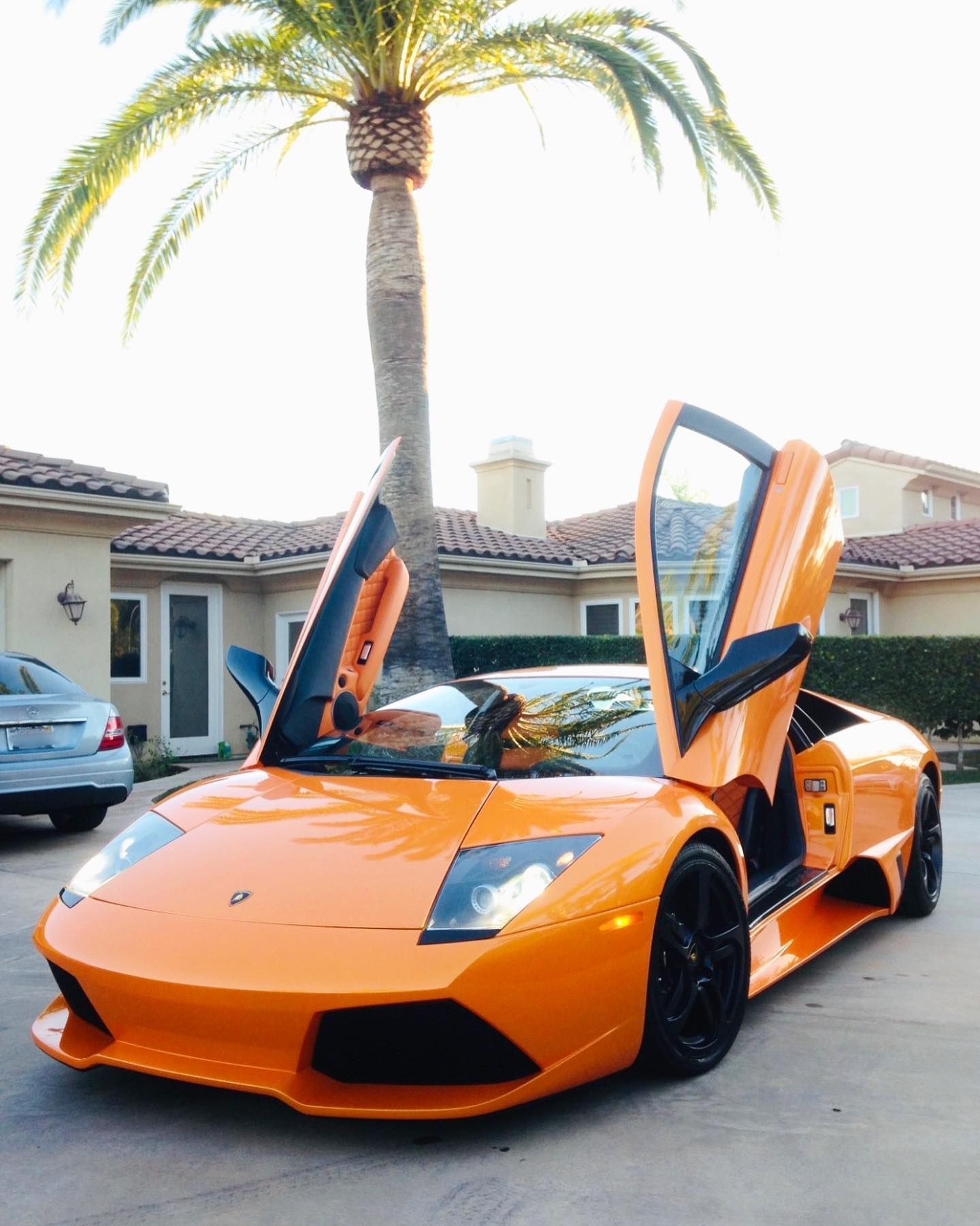 Orange Lamborghini with open doors parked in front of a house.