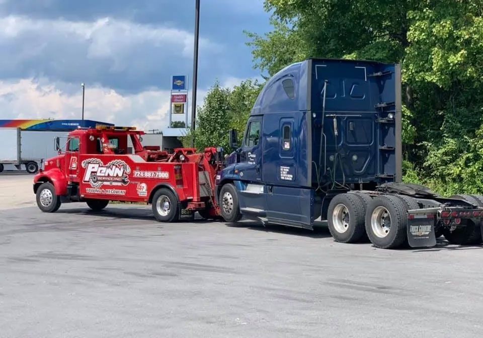 A blue semi truck is being towed by a red tow truck.