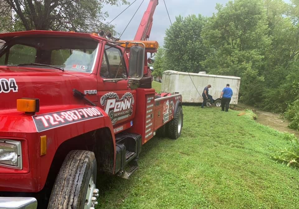 A red tow truck is towing a white trailer in a grassy field.