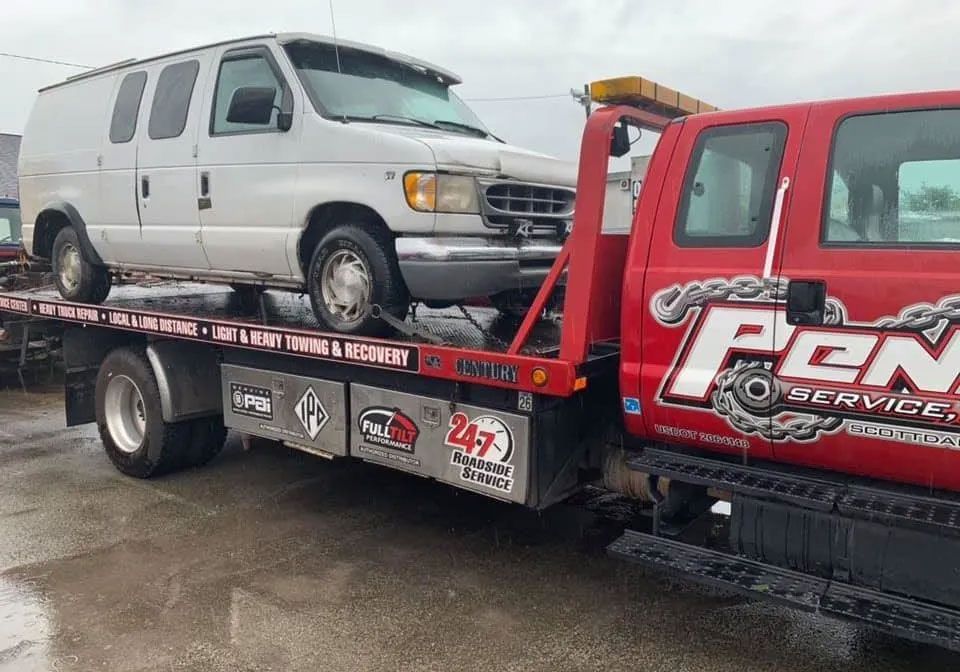 A white van is being towed by a red tow truck.