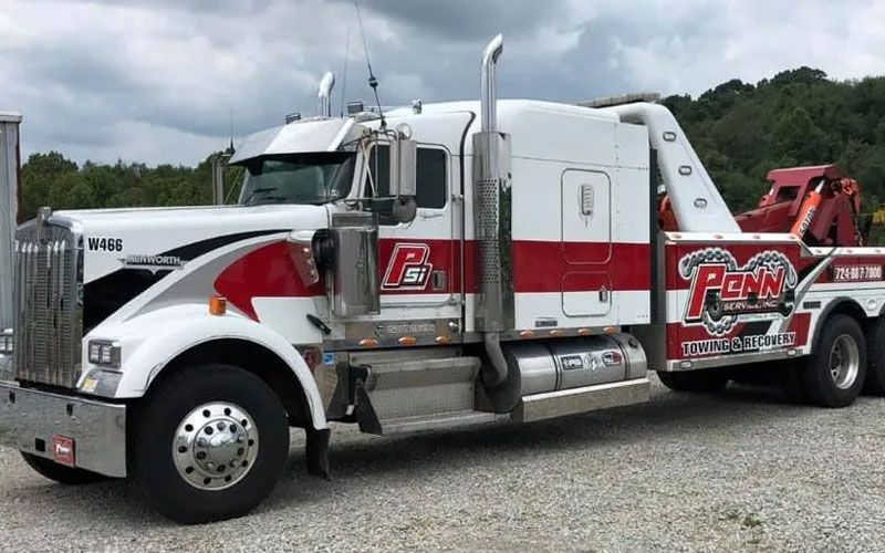 A white and red tow truck is parked in a gravel lot.