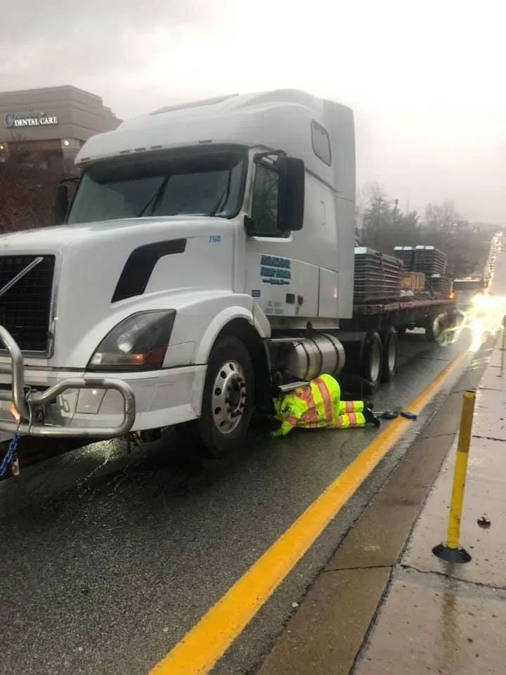 A man is laying on the side of the road next to a semi truck.