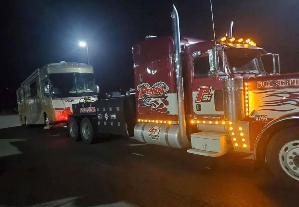 A red tow truck is towing a rv at night.
