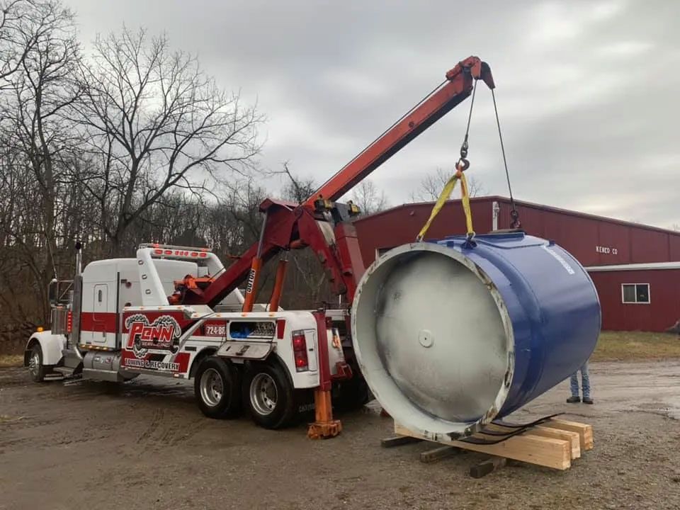 A tow truck is carrying a large blue cylinder with a crane attached to it.
