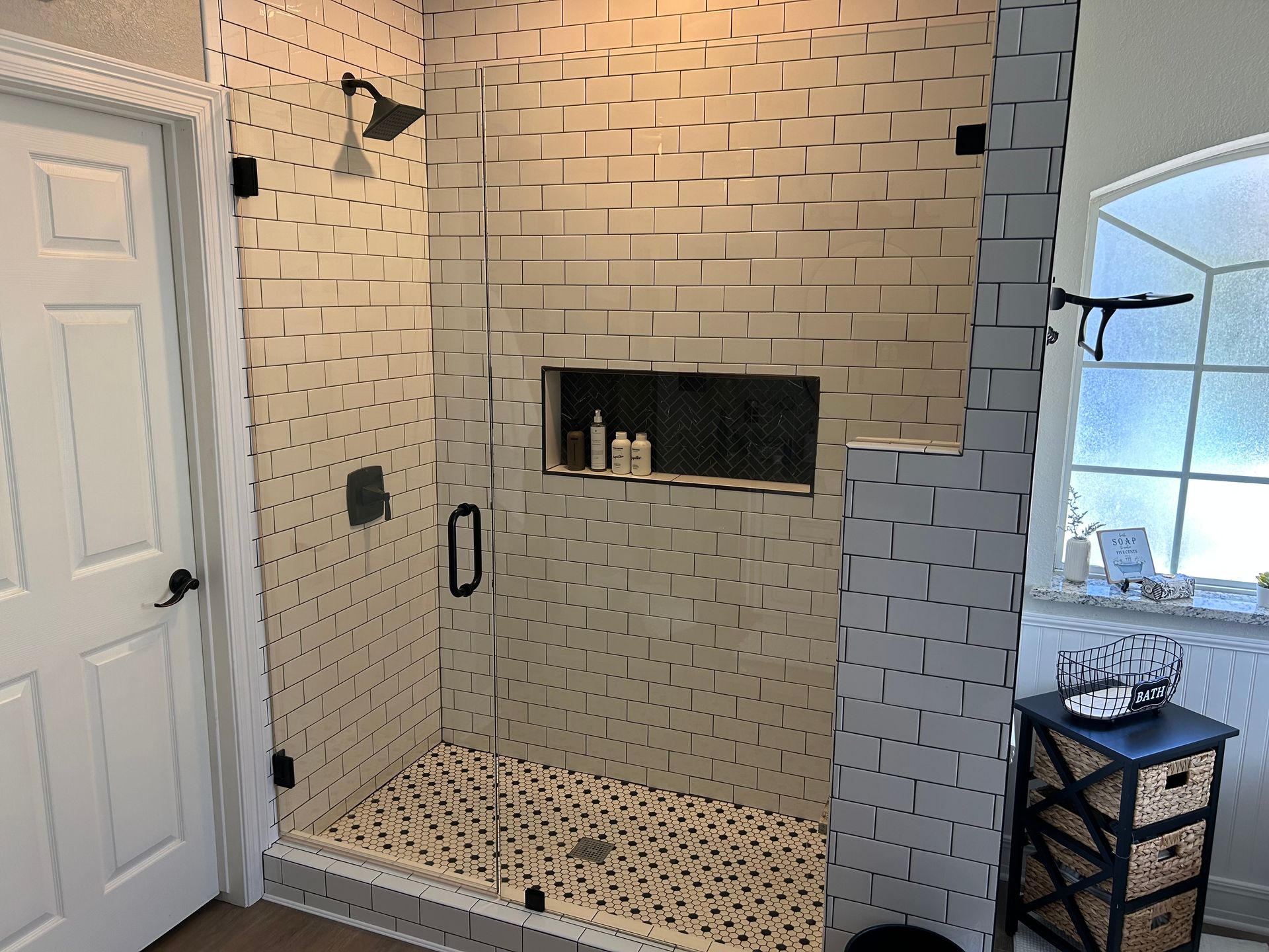 A bathroom with a walk in shower with a glass door and a brick wall.