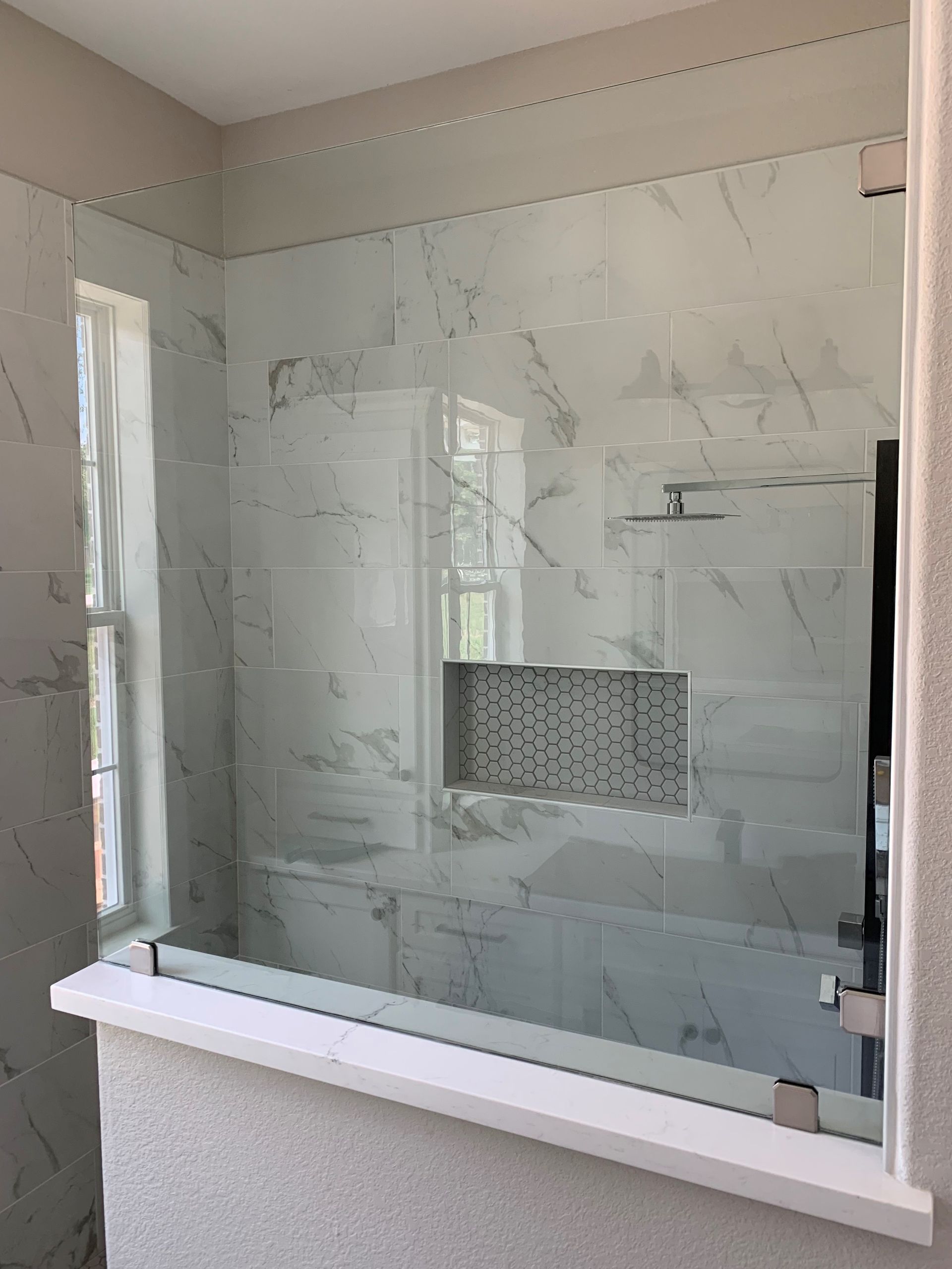 A bathroom with a glass shower door and a window.