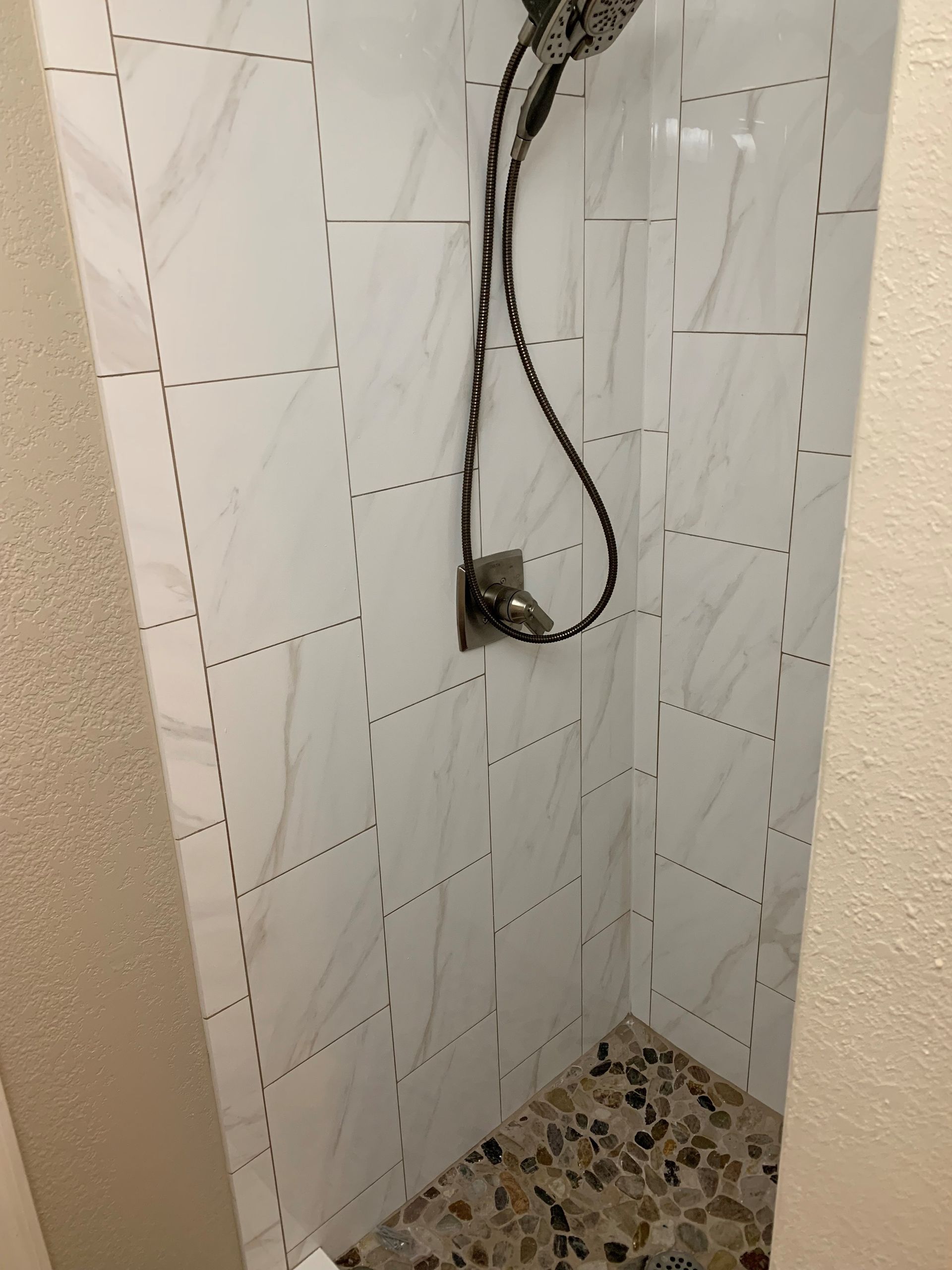 A shower with white tiles and a black shower head