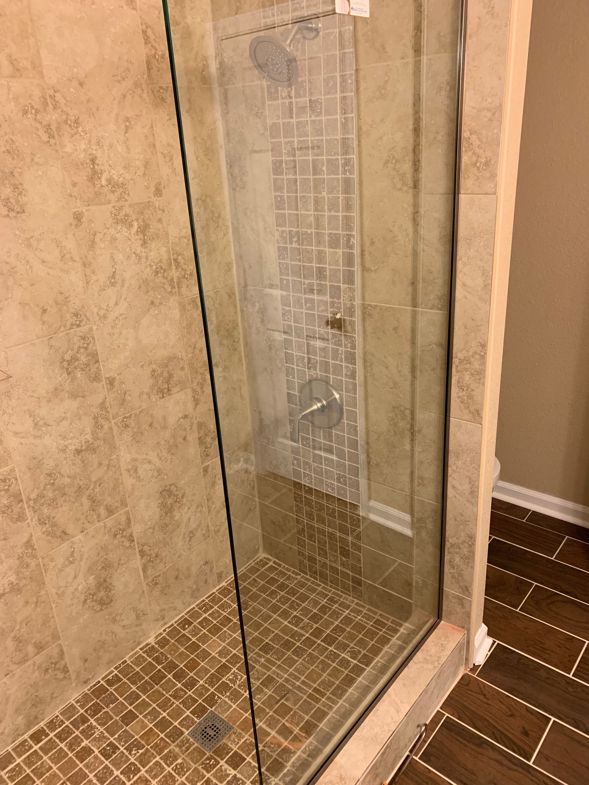 A walk in shower with a glass door and tile floor.