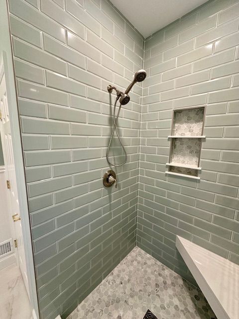 A bathroom with green brick tiles and a walk in shower.