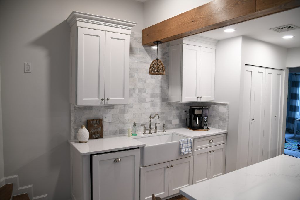 A kitchen with white cabinets, a sink, and a wooden beam
