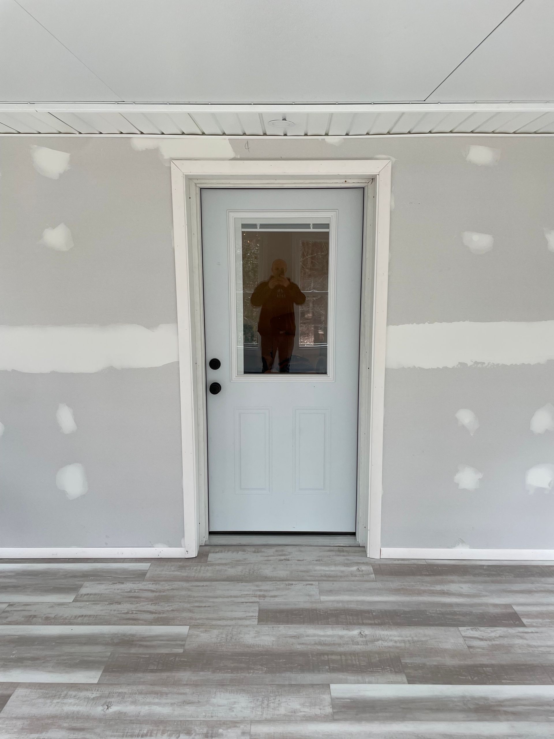 A white door with a window in a room with a reflection of a person in it