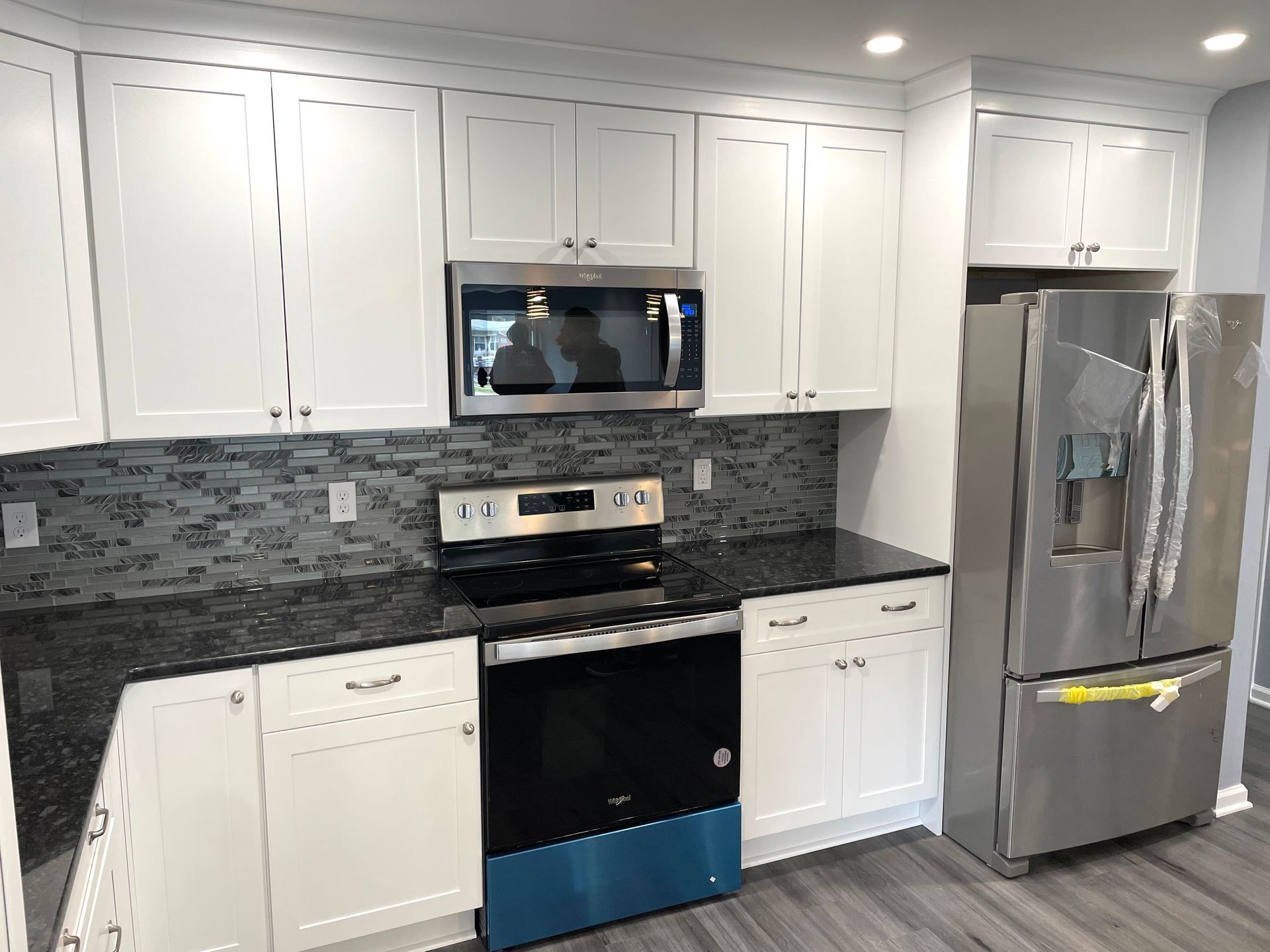 A kitchen with white cabinets, black countertops, a stove, a refrigerator, and a microwave