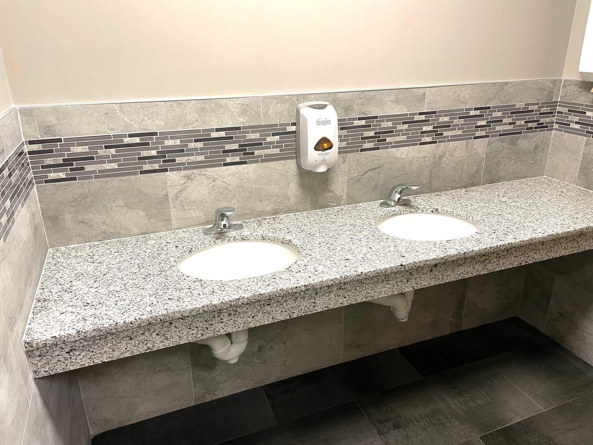 A bathroom with two sinks and a soap dispenser on the wall