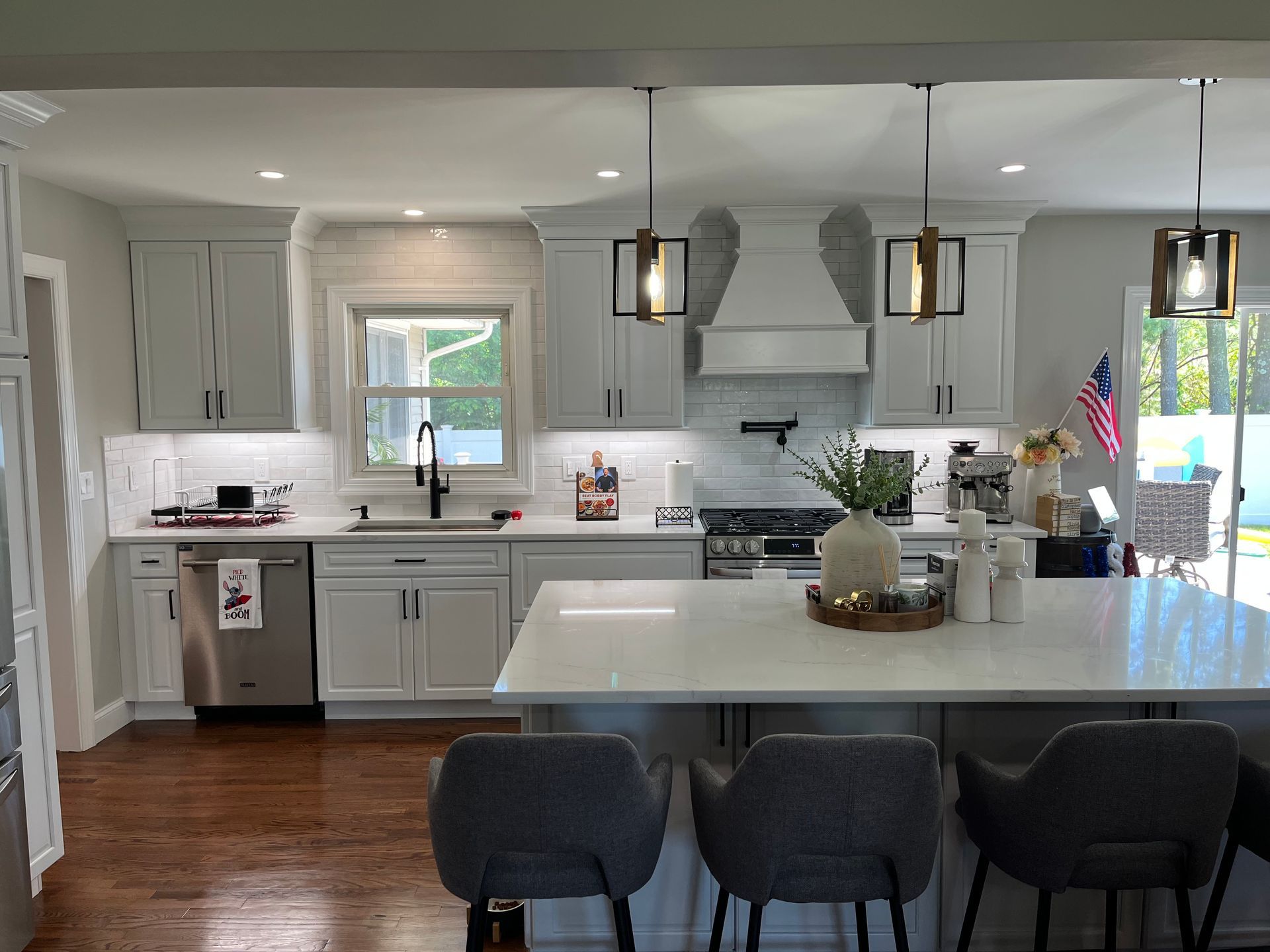 A kitchen with white cabinets, stainless steel appliances, and a large island with lighting fixtures