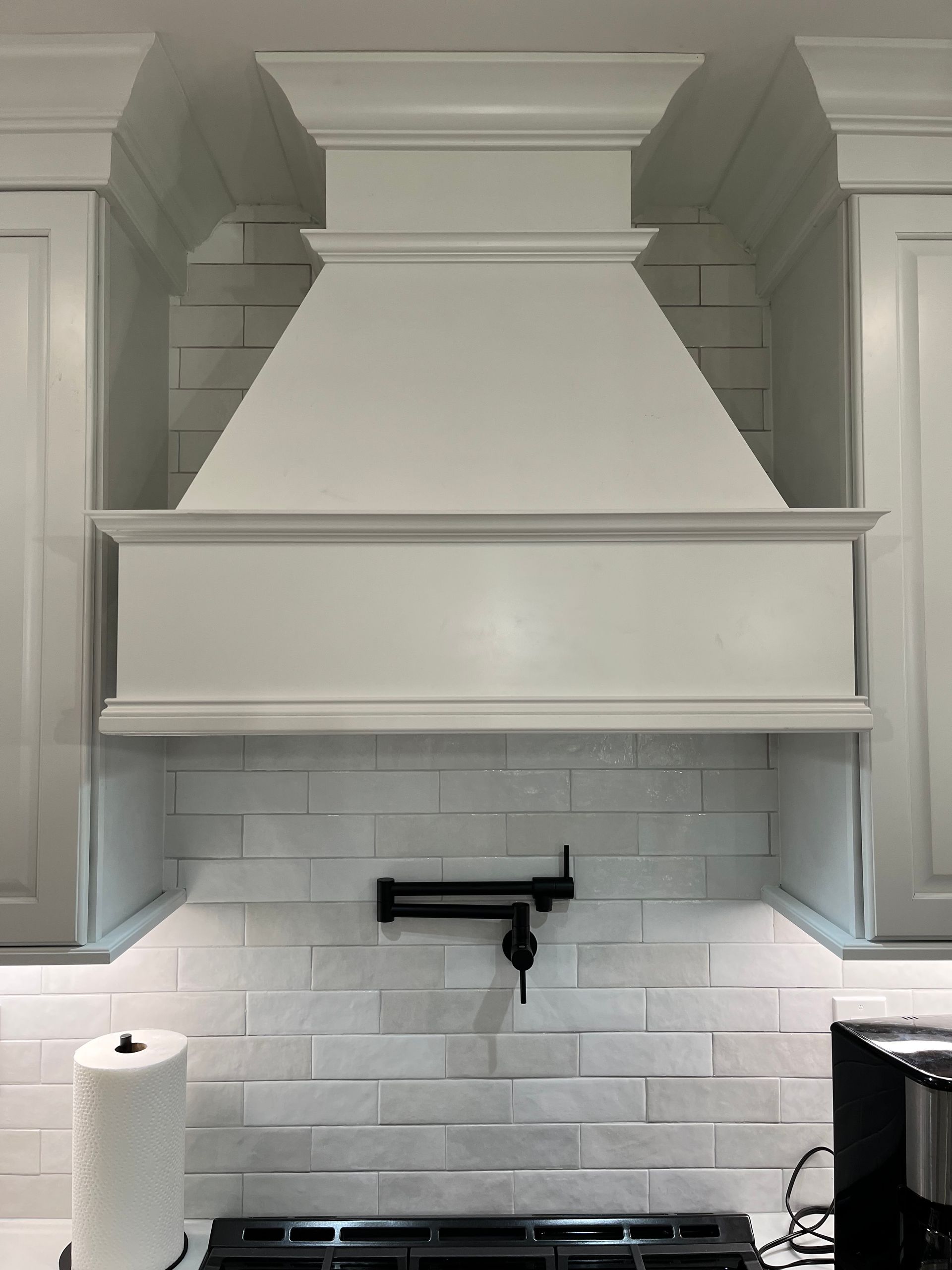 A kitchen with white cabinets and a stove top oven with a hood above it