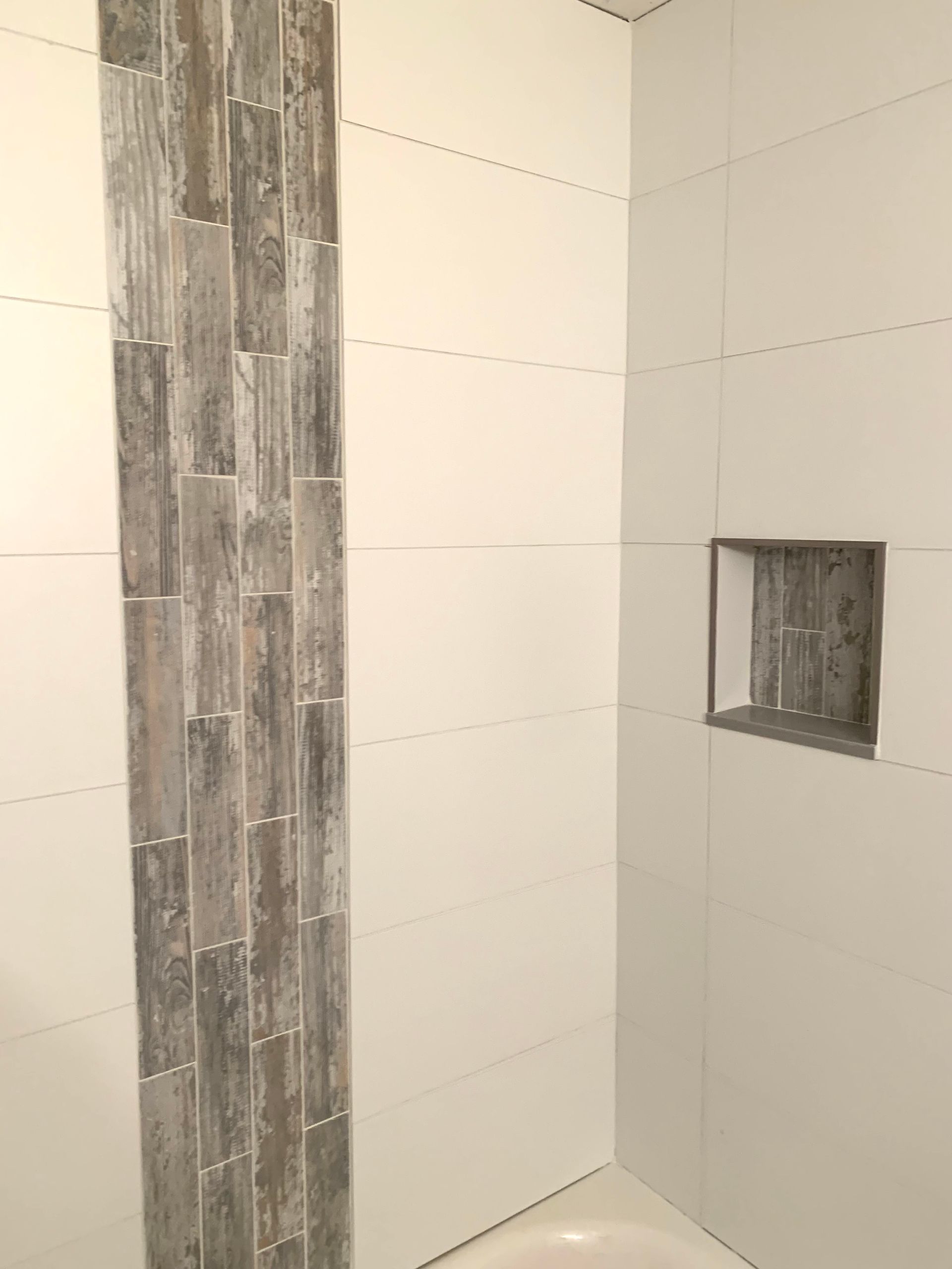 A shower with a gray and white tiles wall and a niche